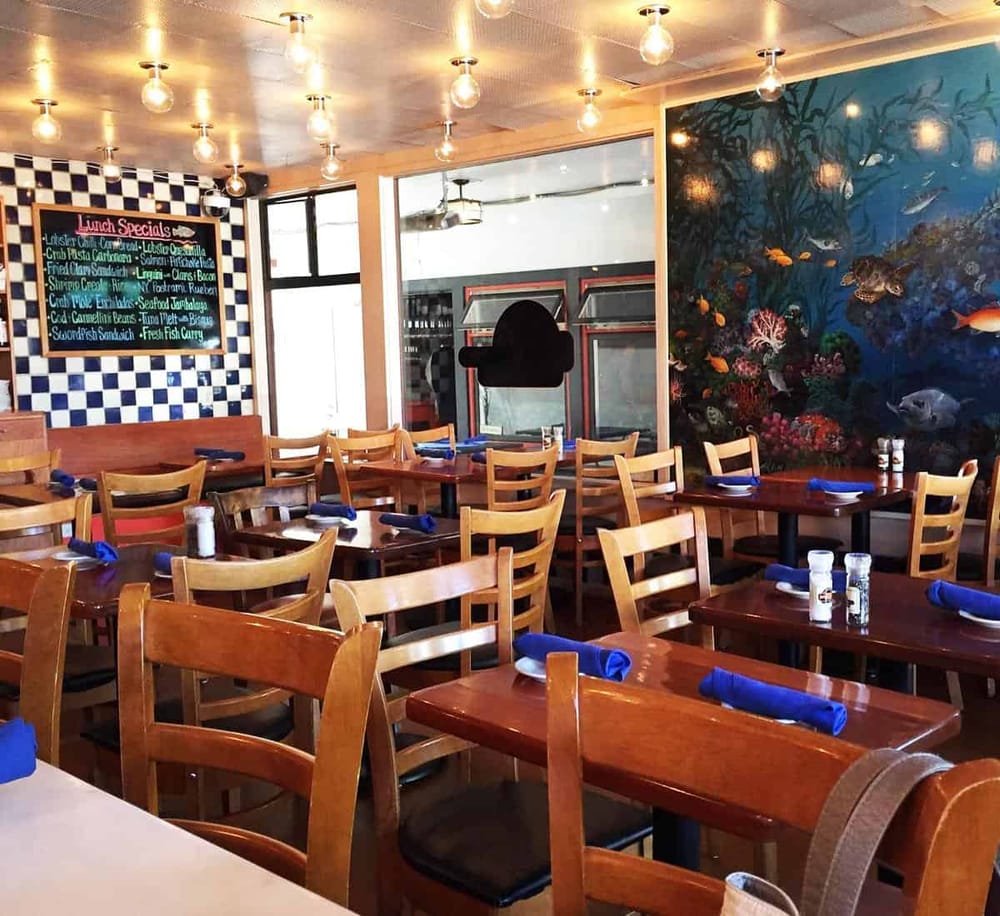 A fish-themed restaurant interior with wooden tables, blue napkins, ocean mural, and ambient lighting for seafood dining experiences.
