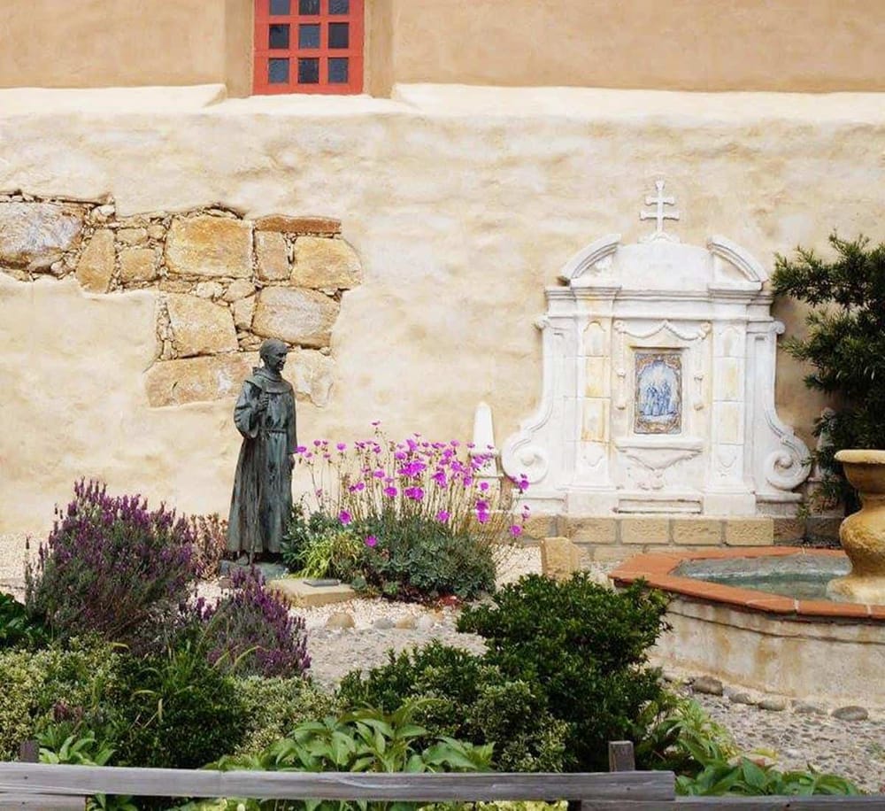 Peaceful historic courtyard with religious statue and stone fountain in Santa Fe, New Mexico.