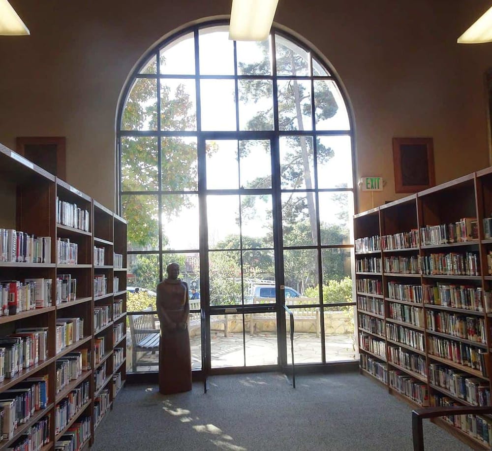 Quiet library interior with large arched window and bookshelves filled with books.