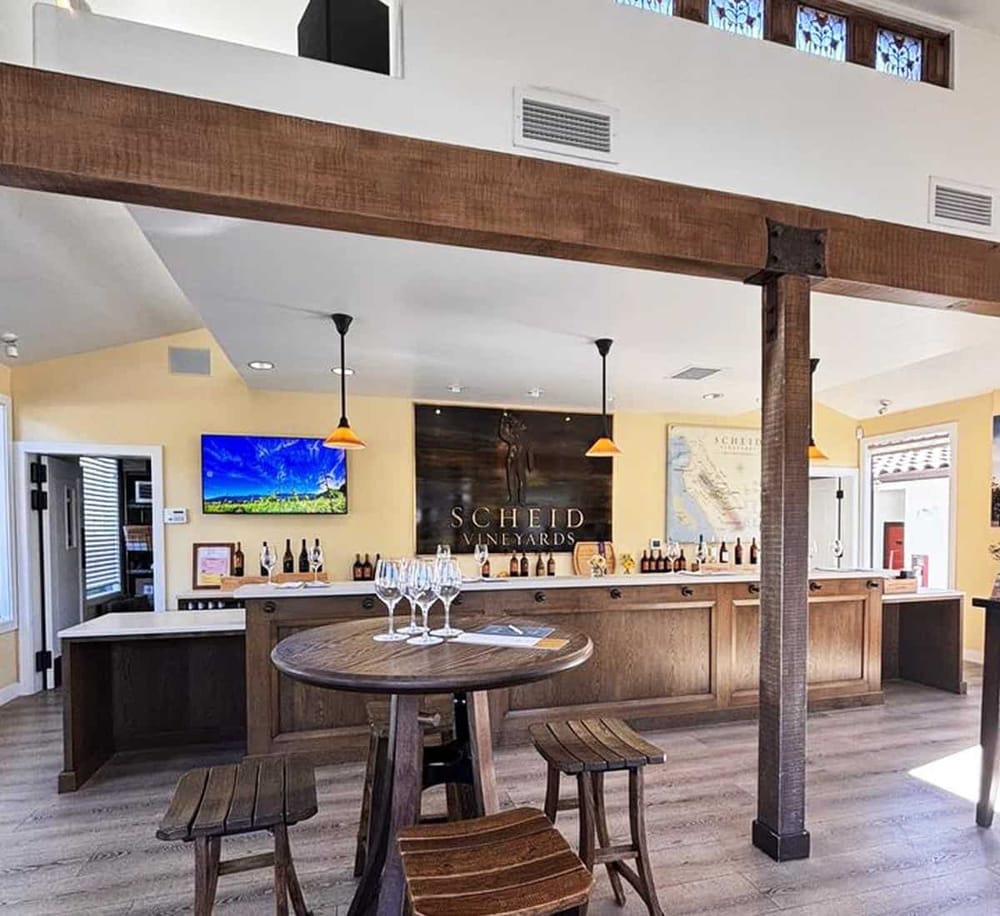 Cozy winery tasting room at Scheid Vineyards with wooden bar, wine bottles, and wine glasses for tasting, inviting wine tourism experience.