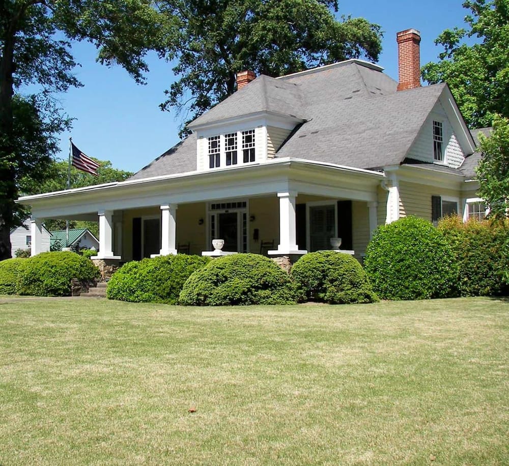Charming American-style house with lush front lawn and classic porch, ideal for homeownership.
