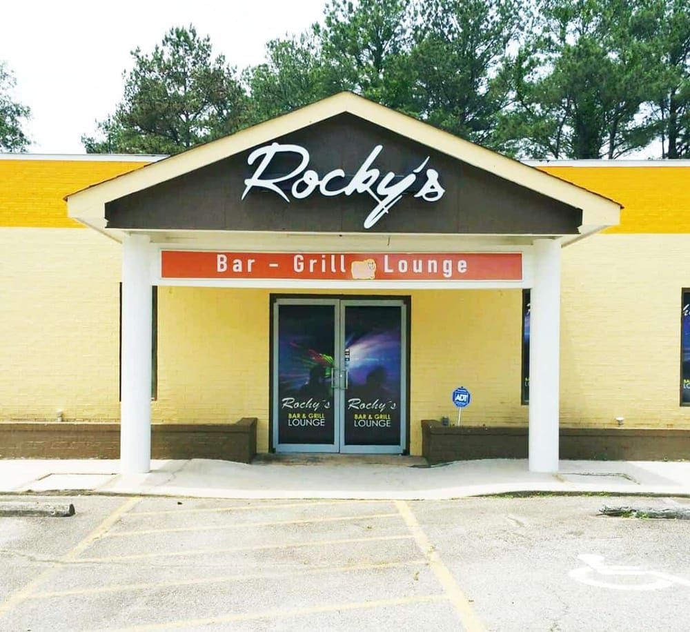 Cozy bar and grill lounge entrance at Rocky's, featuring inviting decor and parking area, ideal for nightlife and dining.