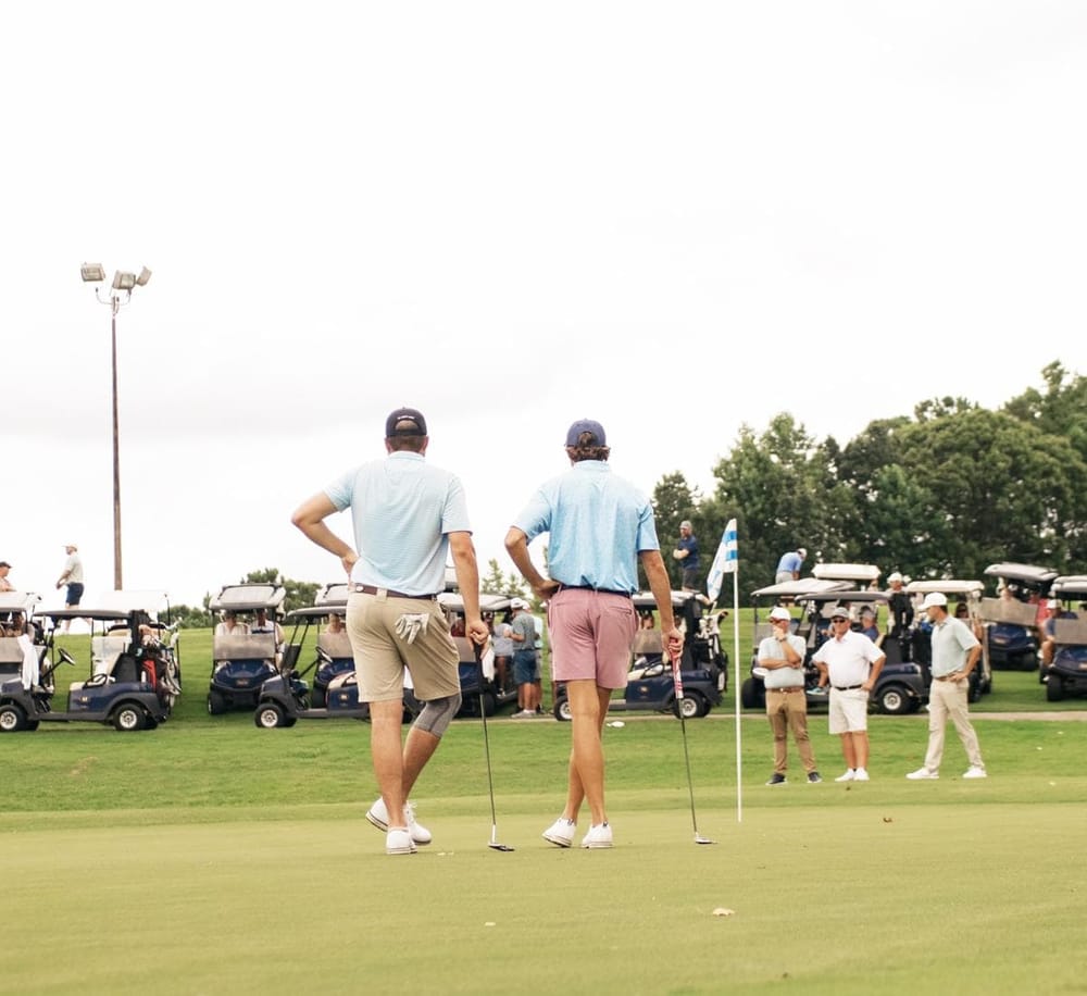 Golf players on the course with a crowd and golf carts in the background, showcasing a golf tournament scene.