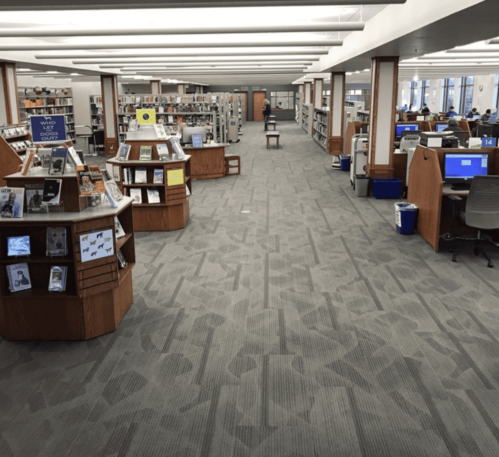 Aisle view of a spacious library with bookshelves, reading areas, and computer stations.