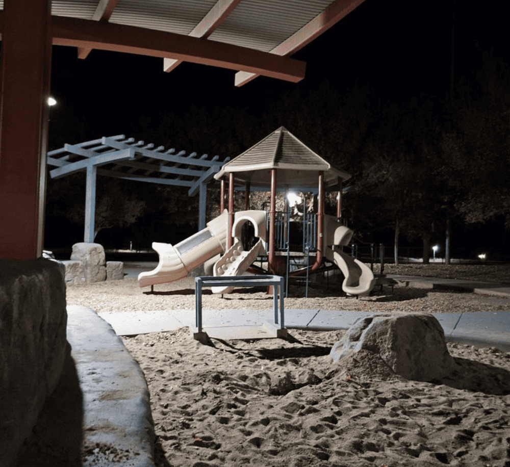 Bright night view of a children's playground with slides and tunnels, illuminated under park lighting.