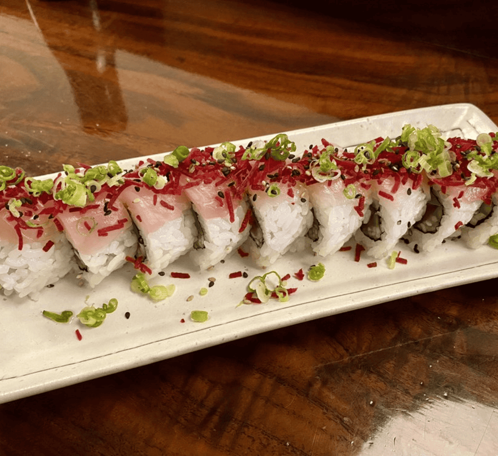 Fresh sushi rolls topped with green onions, red and black sesame seeds on a white platter.