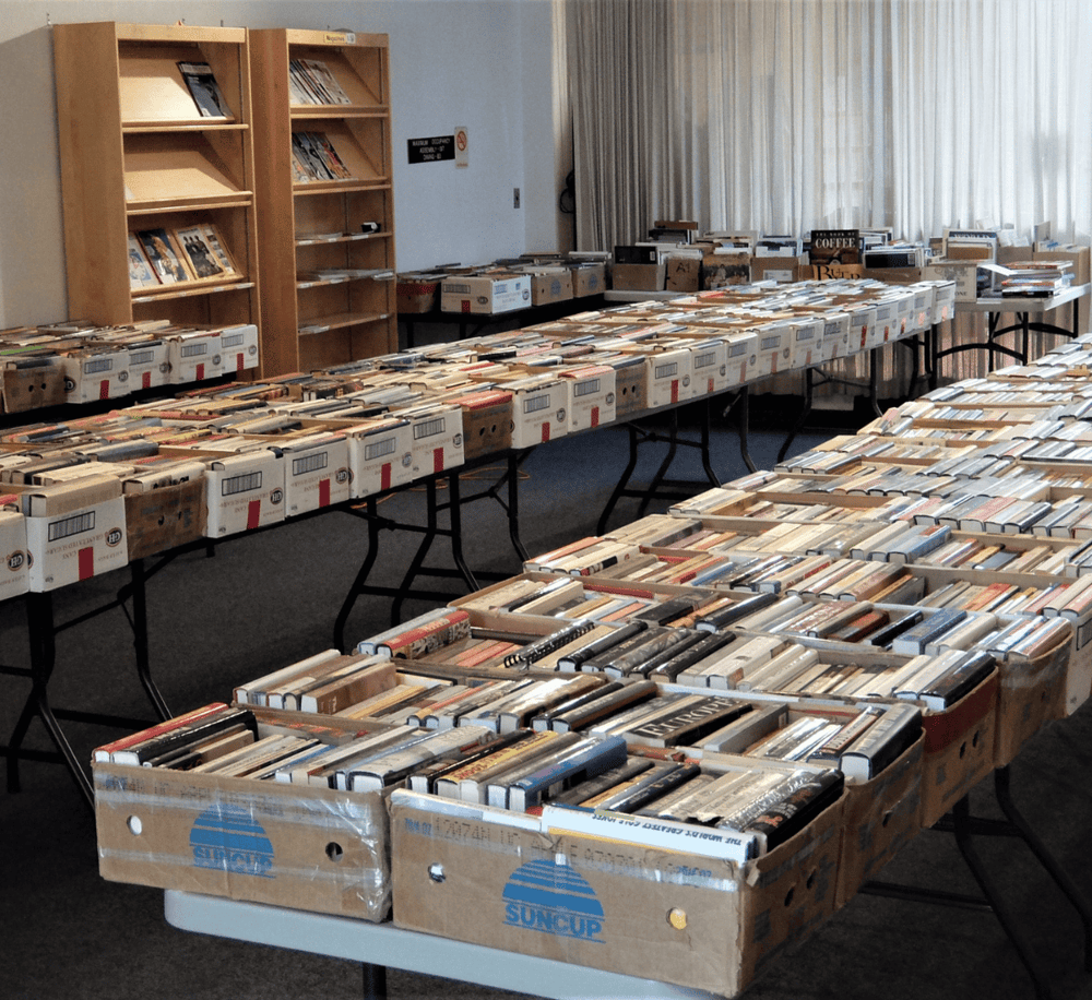 Used books and DVDs organized in boxes at a book sale event for secondhand book shopping and donation.