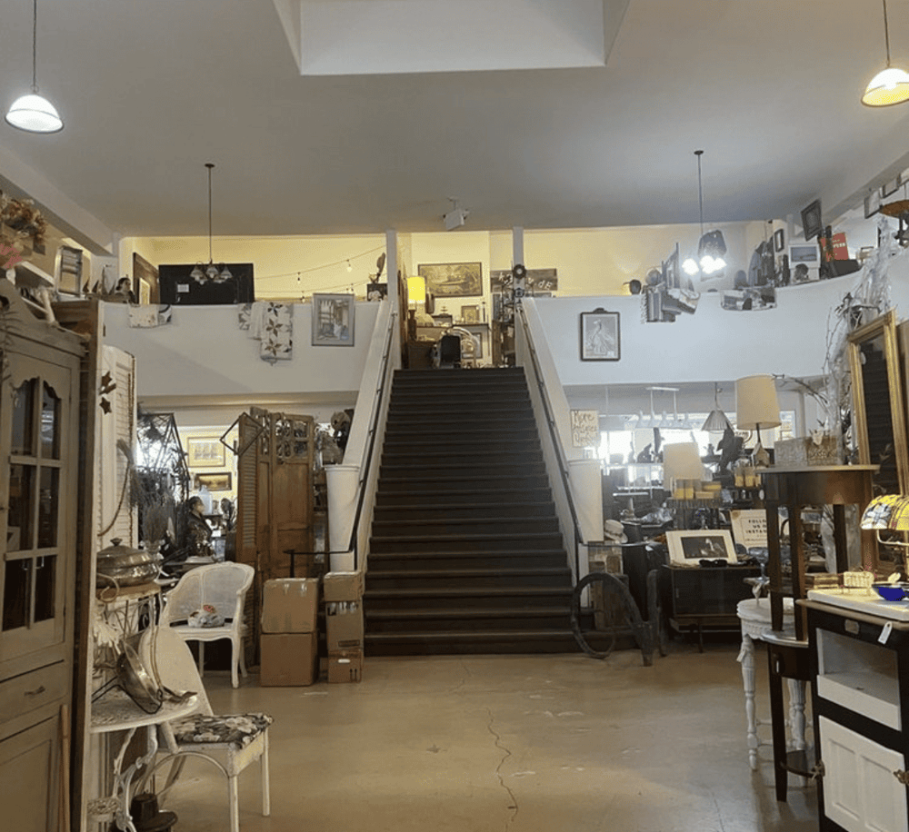 Vintage antique shop interior with staircase, eclectic furniture, and collectibles for sale.