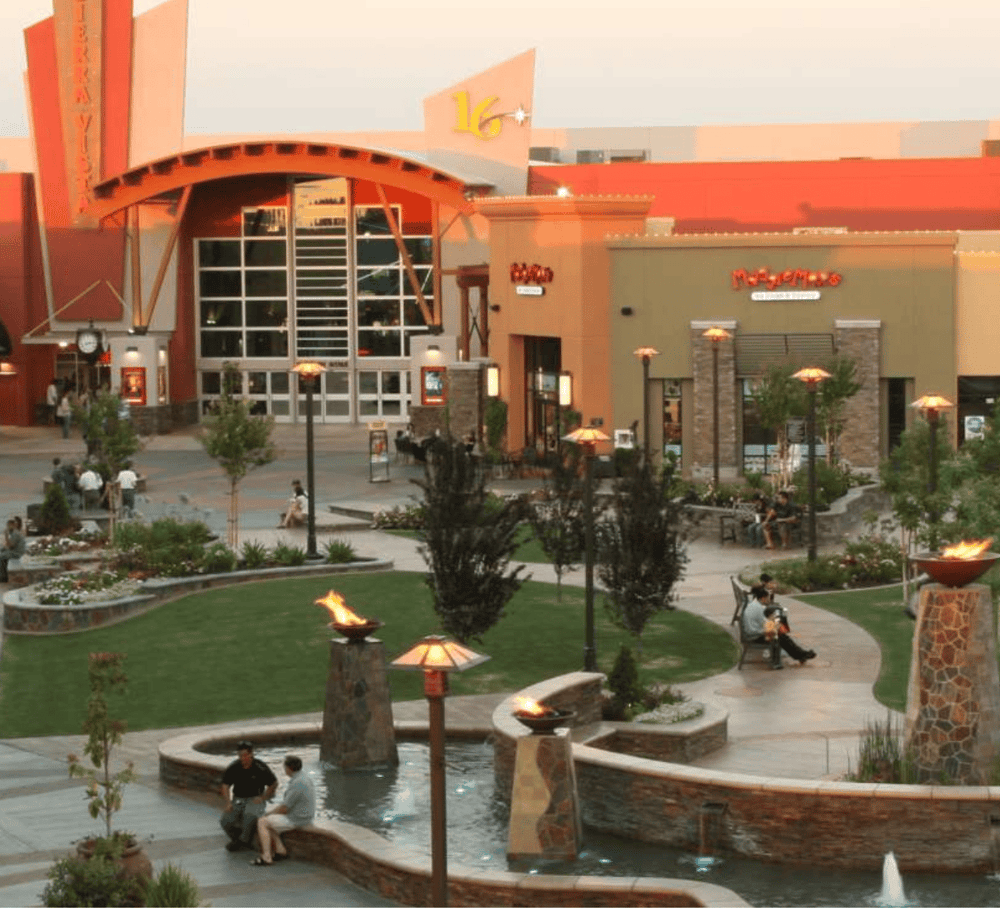 Bright shopping mall exterior with restaurants, outdoor seating, and landscaped areas, perfect for shopping and dining.