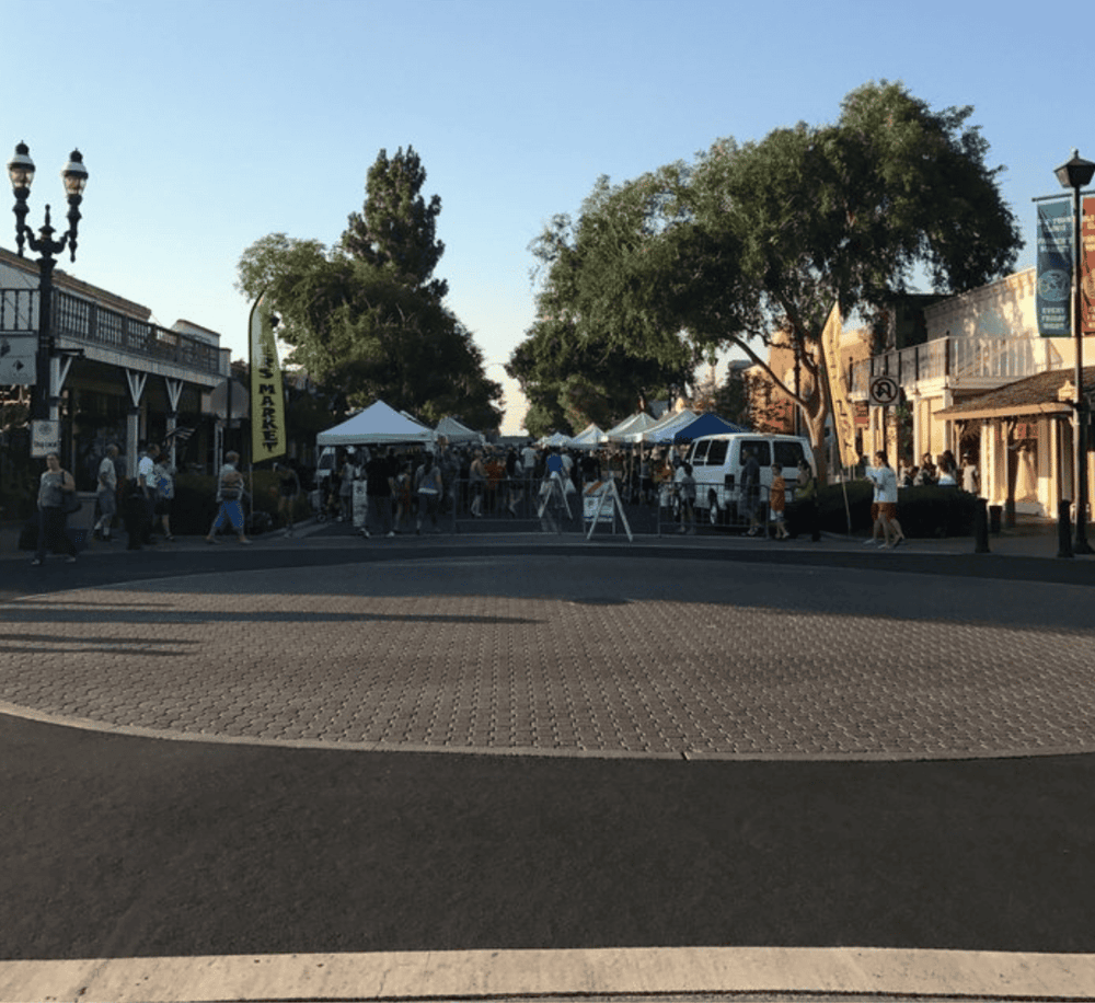Community market event with tents and shoppers in a charming town setting.