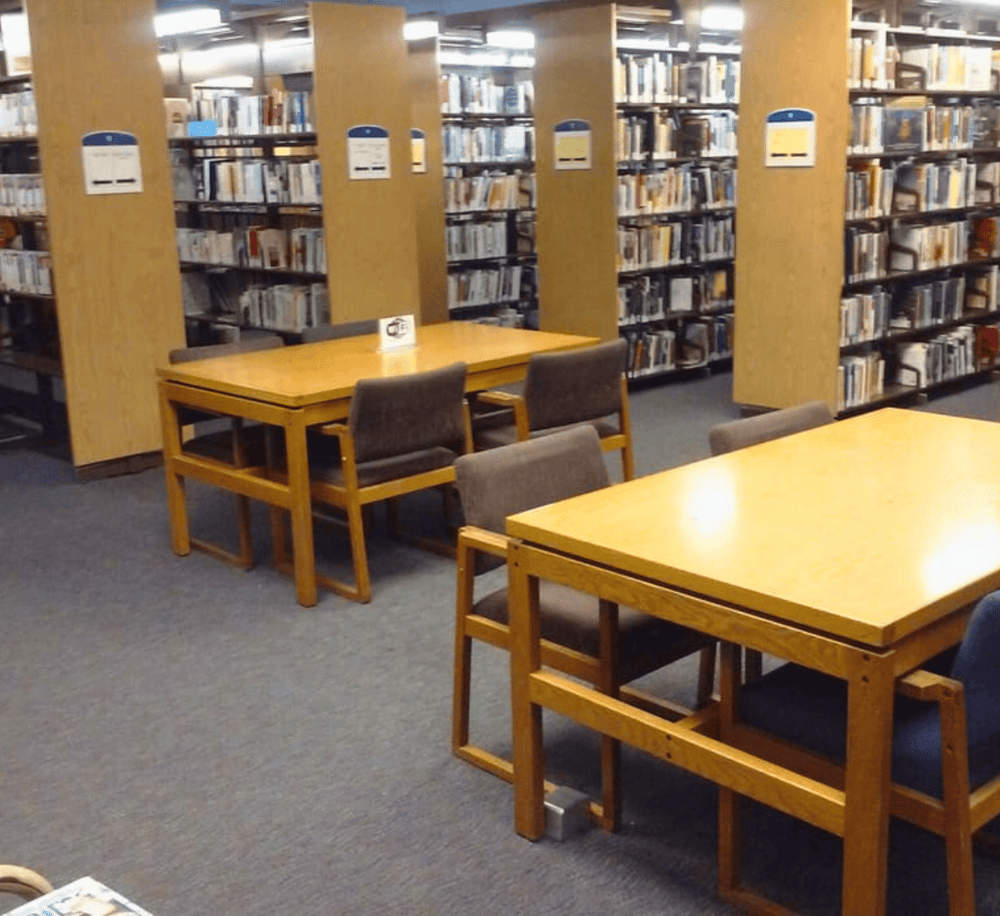 Quiet library study area with wooden tables and bookshelves for research and reading.
