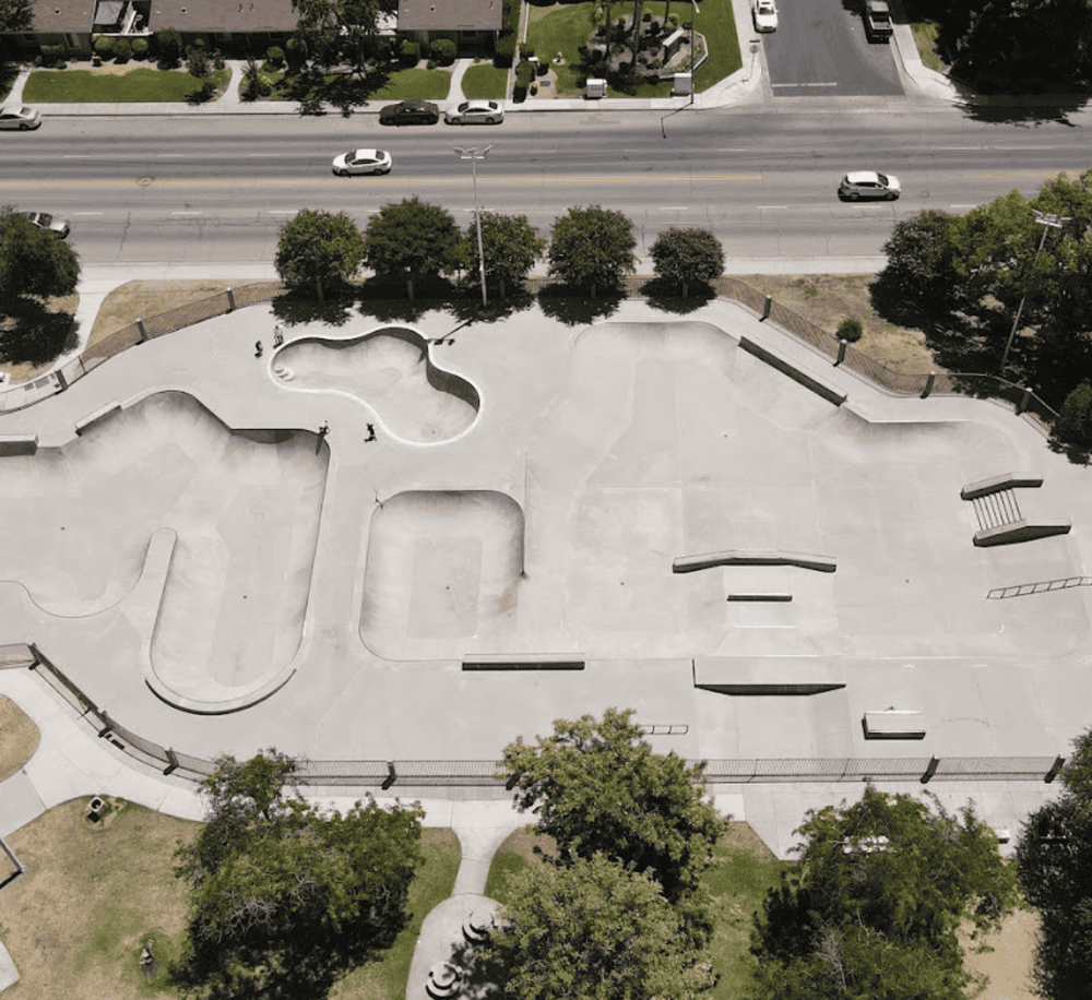 Skatepark with ramps and bowls, surrounded by trees and adjacent to a busy street, ideal for skaters and outdoor recreation.
