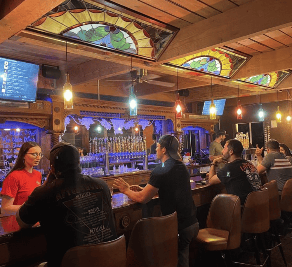 Charming bar interior with stained glass ceilings, colorful pendant lights, and social patrons enjoying drinks.
