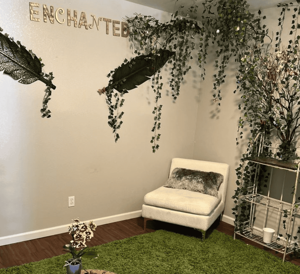 Aesthetic room with greenery decor, white accent chair, and "Enchanted" wall art.