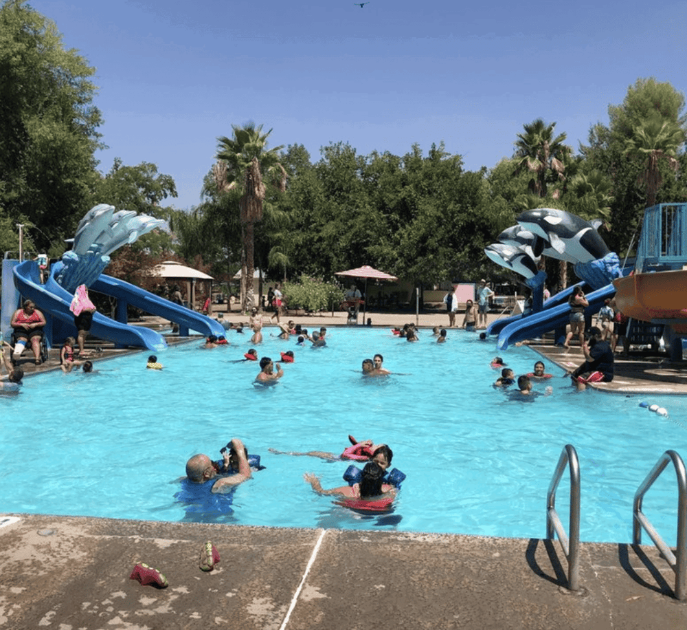 Colorful water slides at a busy outdoor swimming pool with kids and families enjoying a sunny day.