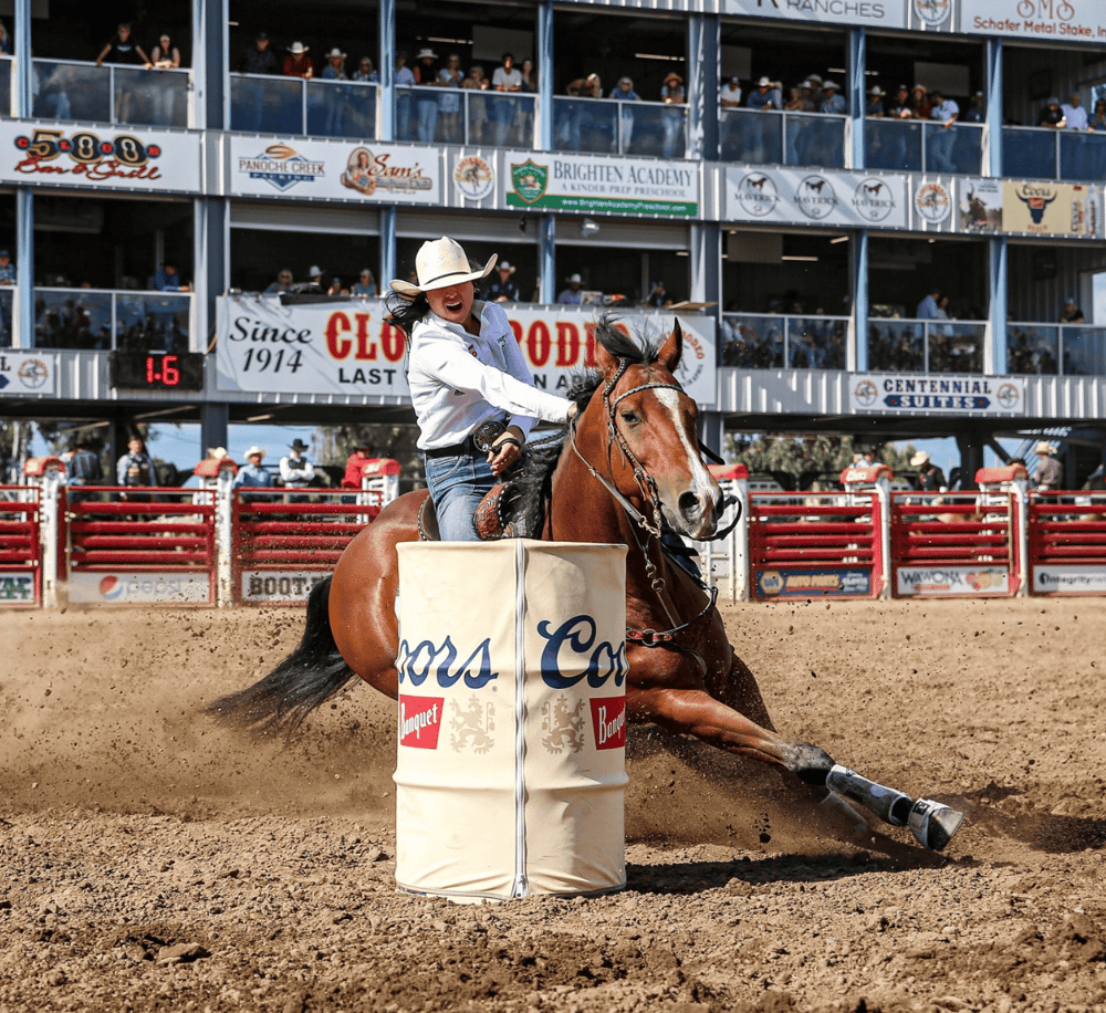 Rodeo rider navigating a barrel race at a professional rodeo event with spectators.