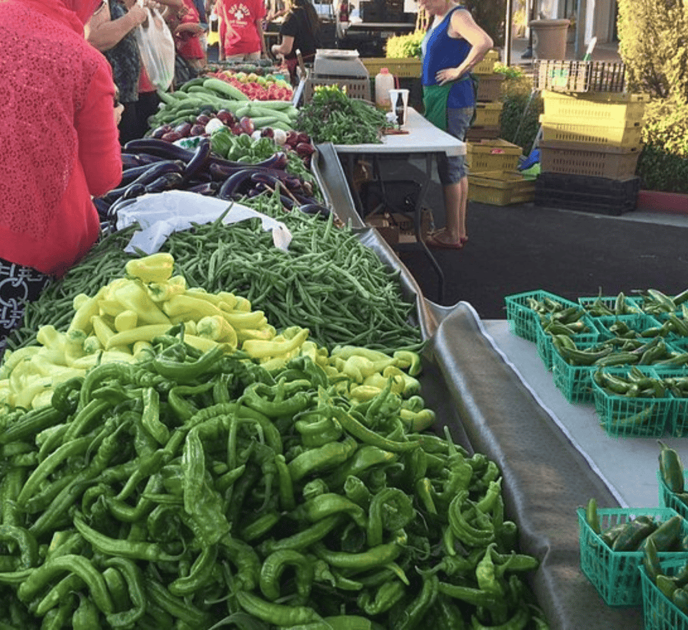Fresh green bell peppers and other vegetables at an outdoor farmers market stall.
