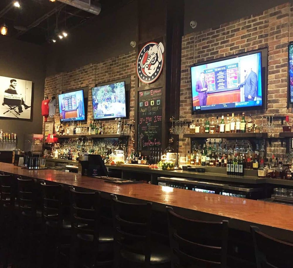 Cozy bar interior with exposed brick walls, multiple TVs, and extensive liquor selection for nightlife entertainment.