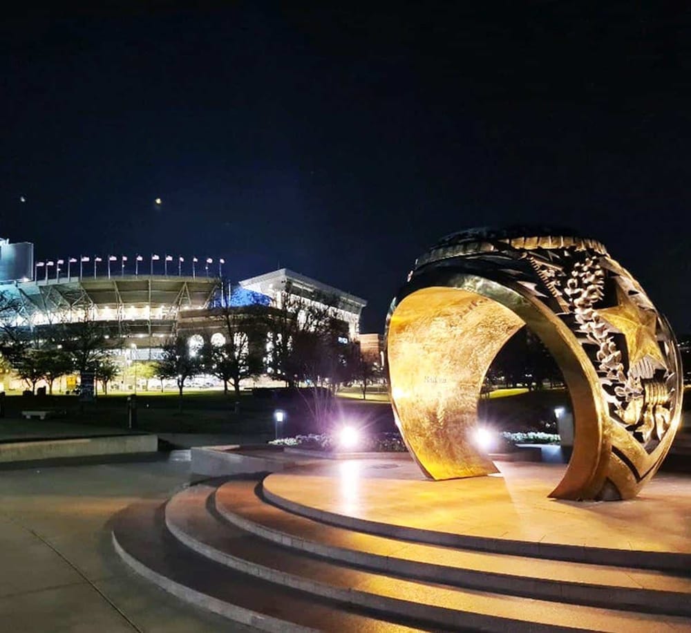 Contemporary bronze sculpture illuminated at night near a modern stadium, showcasing public art and urban design.