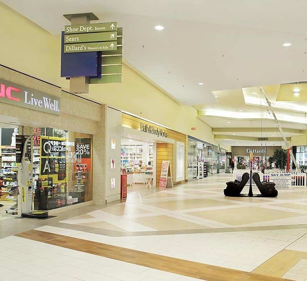 Bright shopping mall corridor with store signage and directional signs for stores and services.
