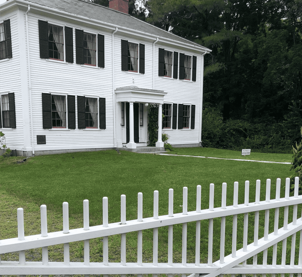 White historic house with black shutters, lush green lawn, and white picket fence, part of QuestForDirections' historical site collection.