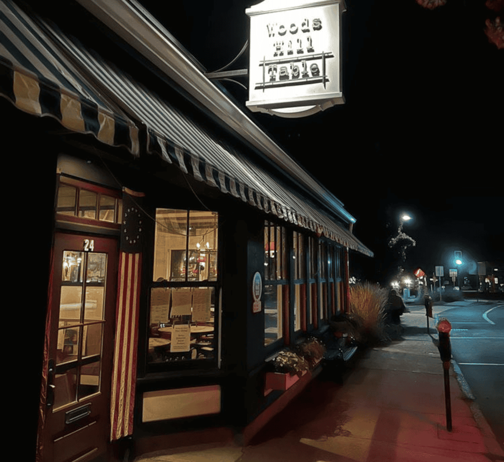 Nighttime exterior view of a cozy cafe or restaurant with large windows and striped awning.