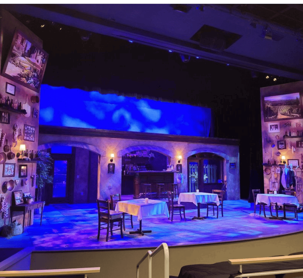 A cozy restaurant stage with purple and blue lighting, decorated with pictures, bottles, and vintage decor. Perfect for live performances.