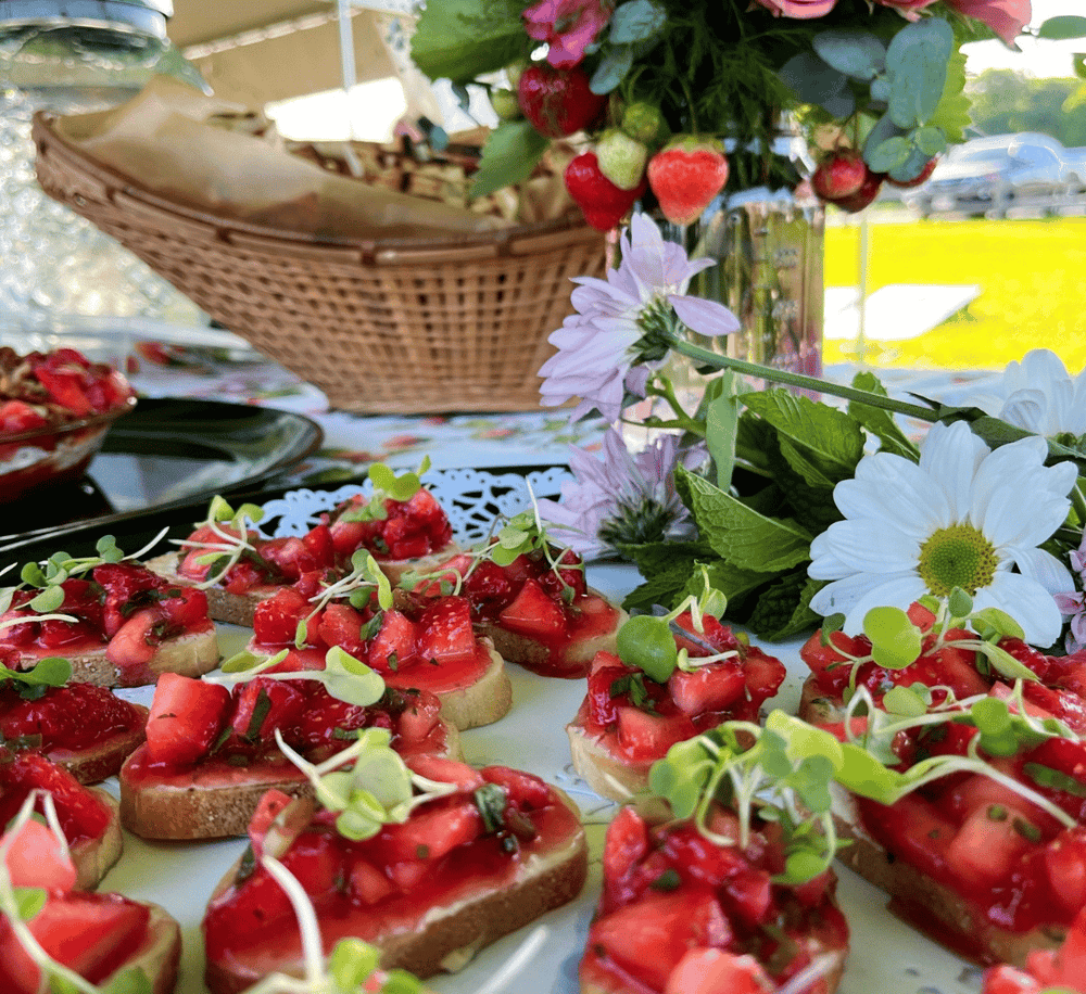 Fresh strawberry and basil bruschetta at outdoor event with flowers and picnic setup.