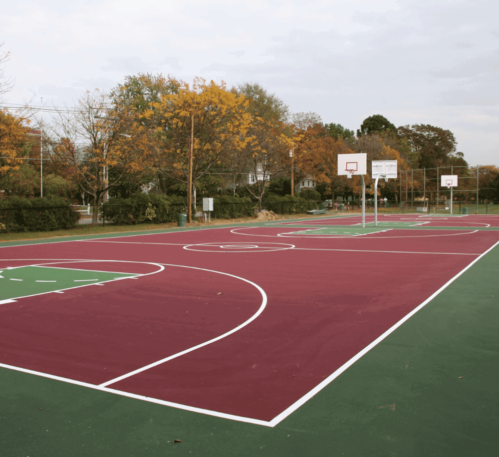 Wide view of a colorful outdoor basketball court in a park during fall, surrounded by trees with autumn leaves.