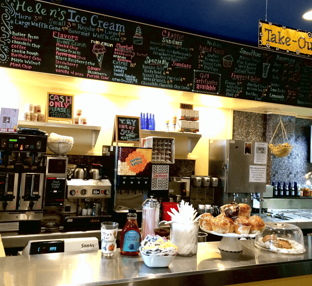 Warm coffee shop counter with baked goods and colorful menu blackboard in the background.