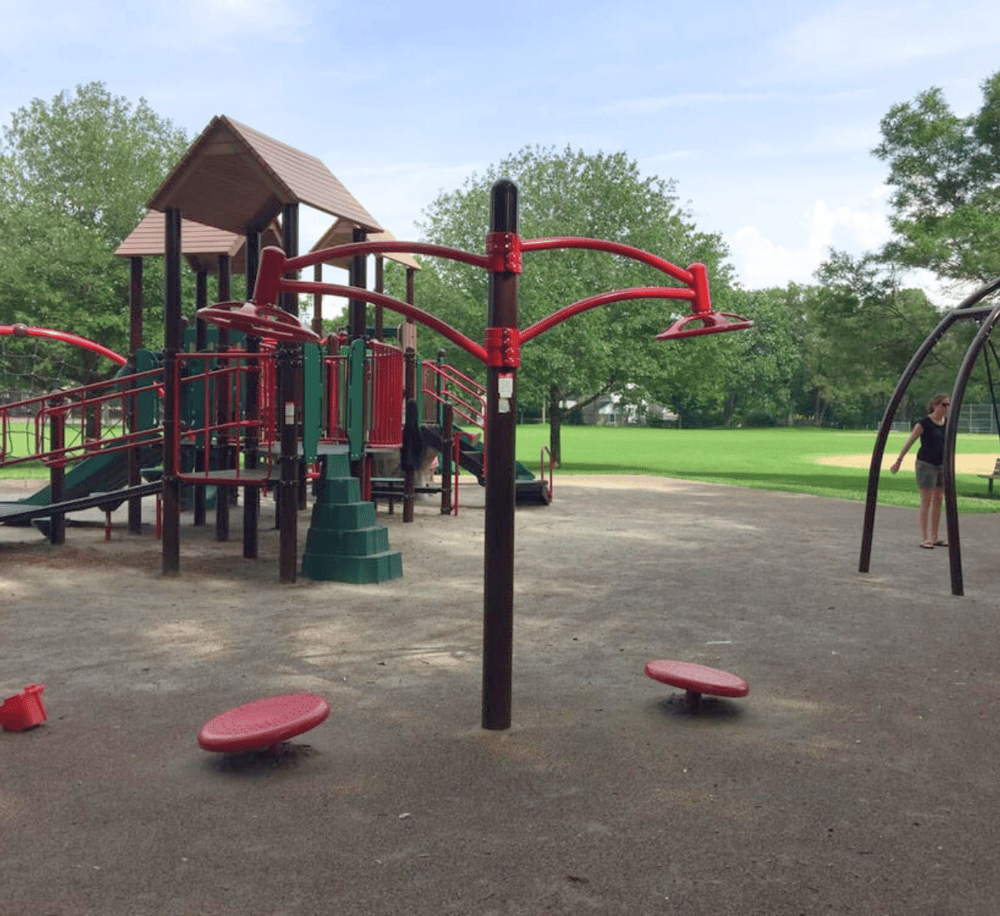 Colorful playground equipment in a park with green trees and open grassy area.