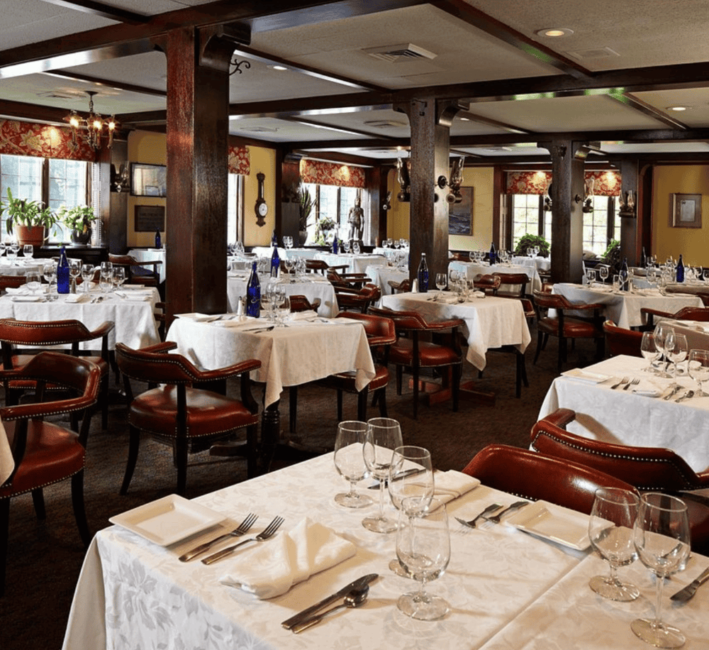 Elegant restaurant dining room with white tablecloths, wine glasses, and traditional decor.