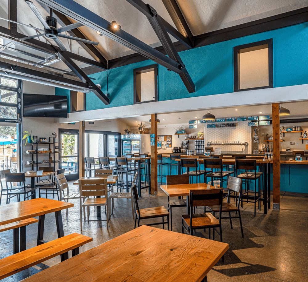 Modern brewery interior with wooden tables, bar seating, and vibrant blue accents for a welcoming atmosphere.