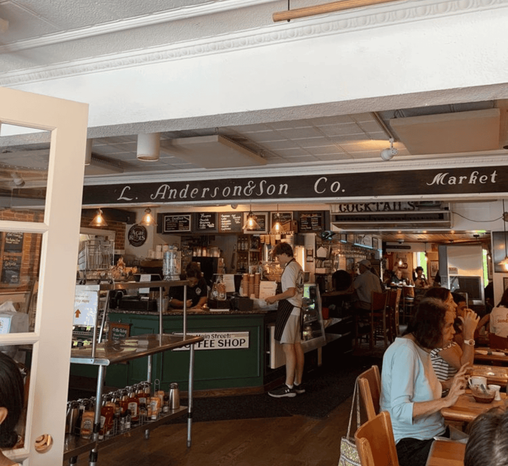 Warm coffee shop interior at L. Anderson & Son Market with customers enjoying drinks.
