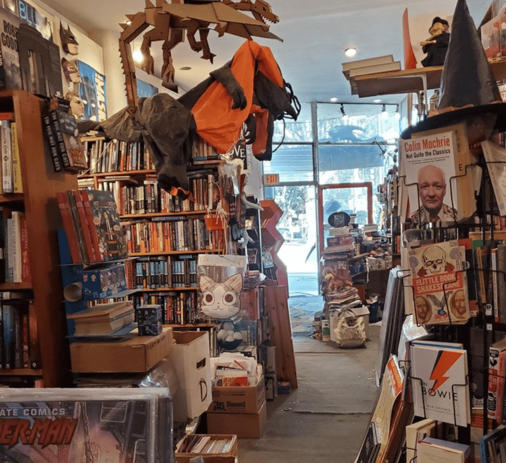 Aisle of eclectic books and collectibles at QuestForDirections, a vintage bookstore in Spokane. Explore a vast selection of comics, novels, and rare finds.