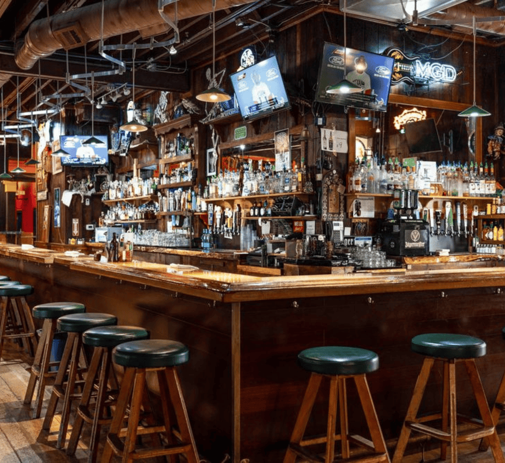 Cozy rustic bar with wooden stools, multiple TV screens, and extensive liquor selection for a vibrant nightlife experience.