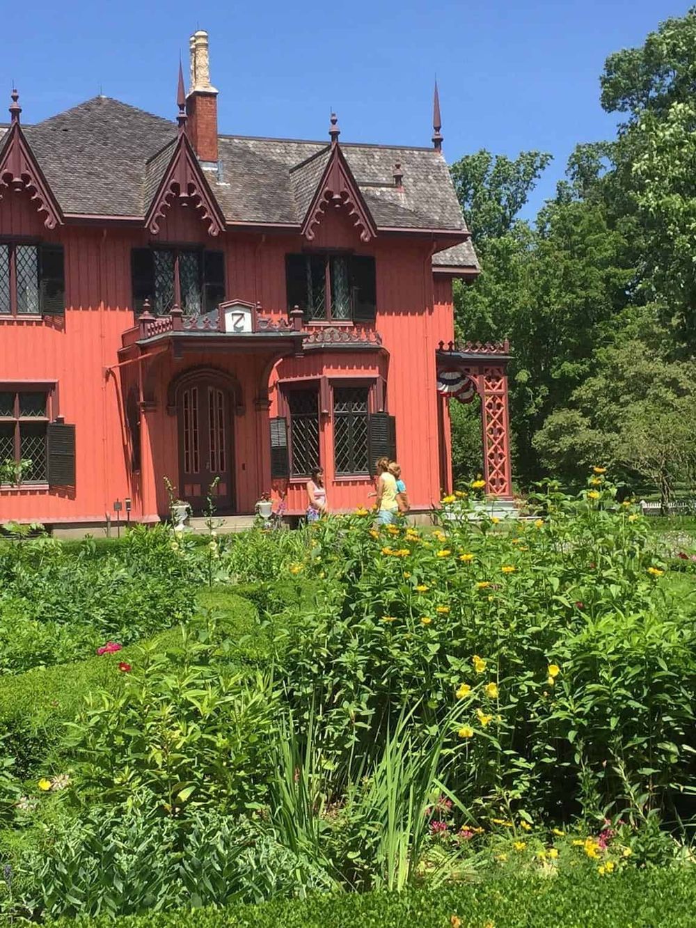 Colorful Victorian house surrounded by lush garden and flowers, showcasing scenic views and unique architecture.