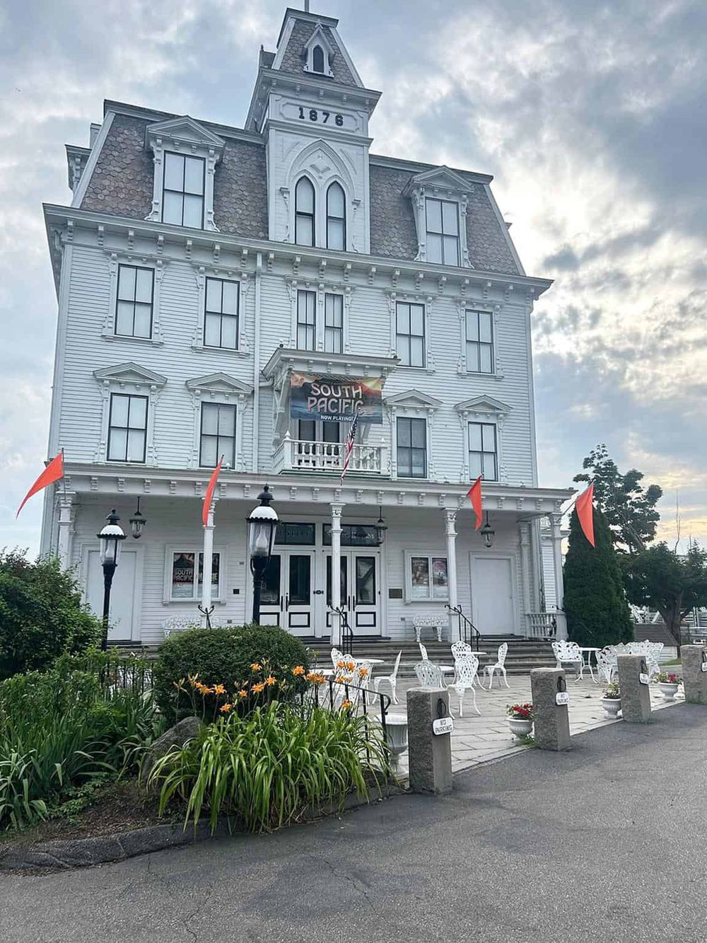 Victorian-style building with a "South Pacific" theater sign, white exterior, decorative iron chairs, and garden in front.