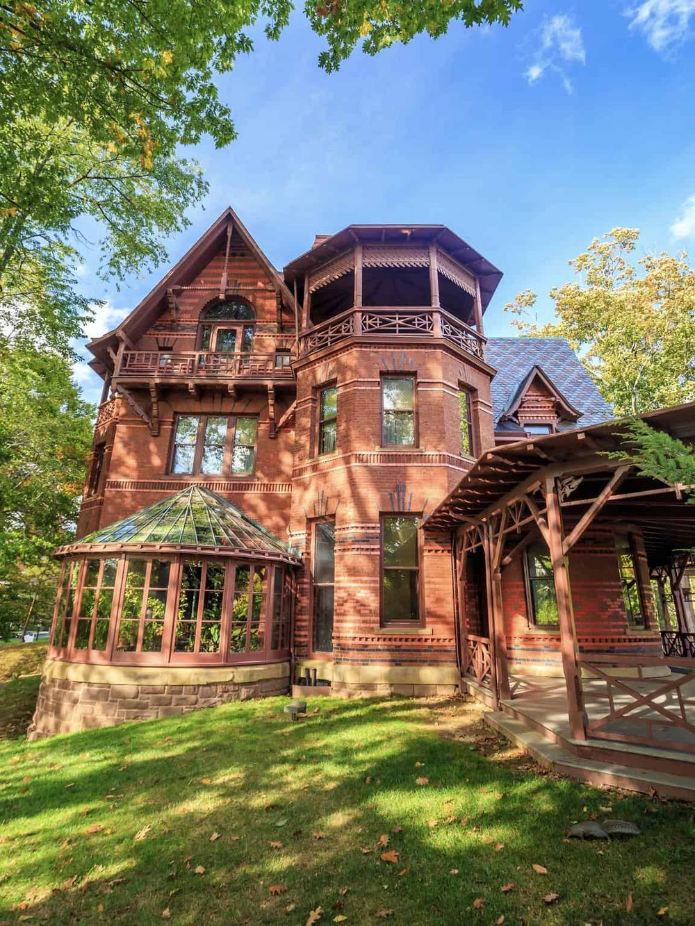 Old Victorian-style house in lush green garden with clear blue sky and vibrant trees.