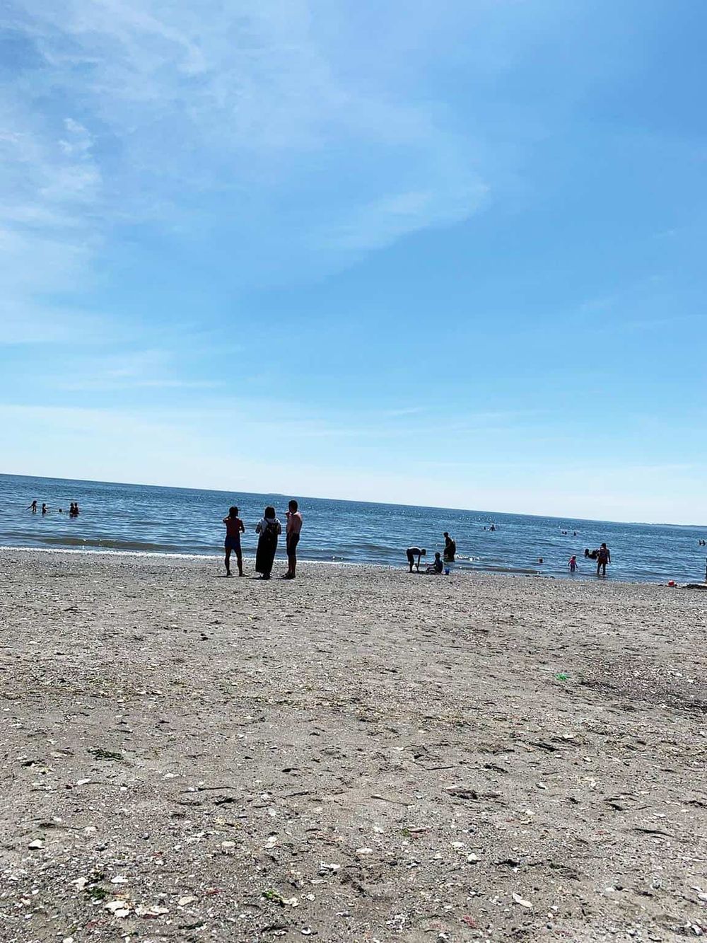 Beach scene with people enjoying the ocean, blue sky, and sandy shoreline, ideal for travel and leisure.