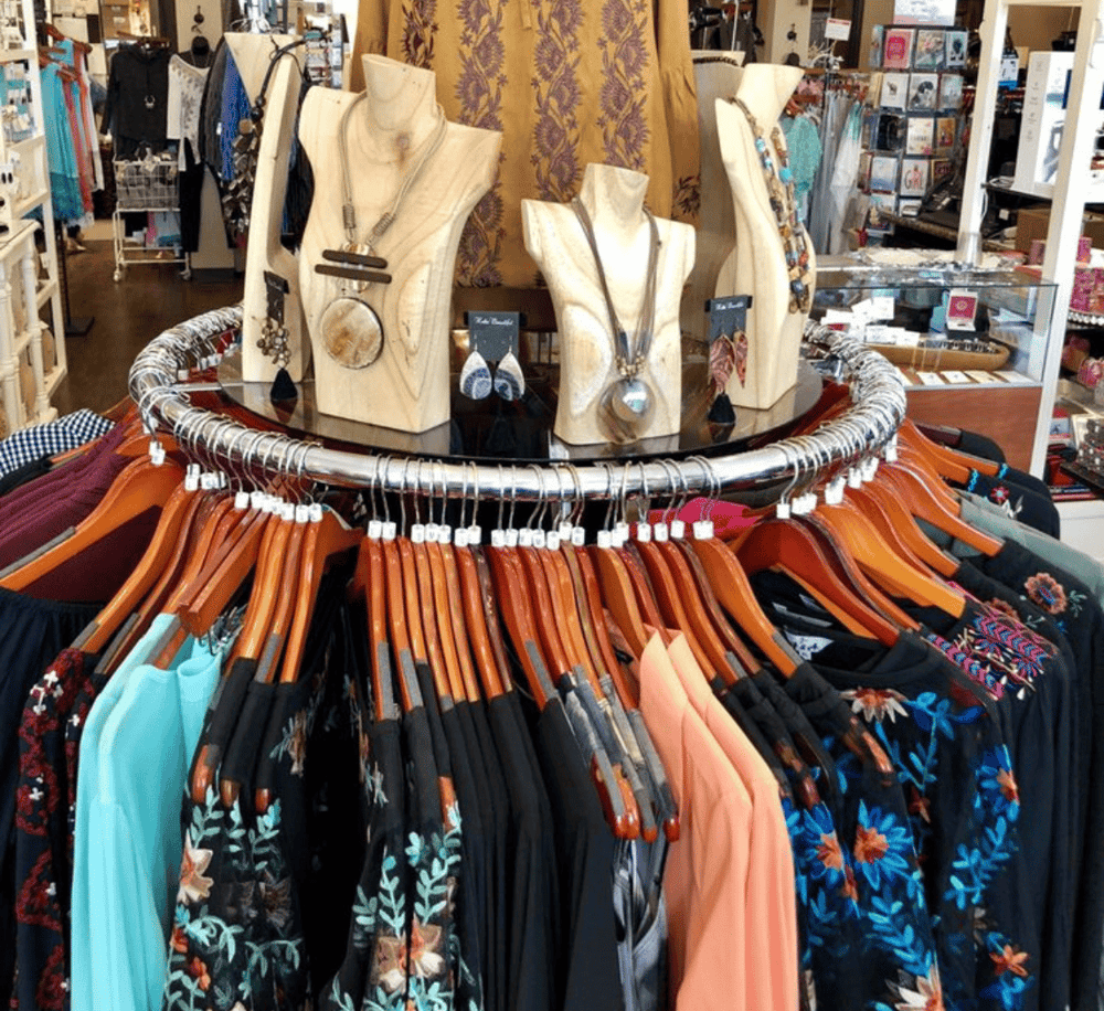 Colorful boutique clothing rack with jewelry displays and accessory mannequins, inside a retail store.
