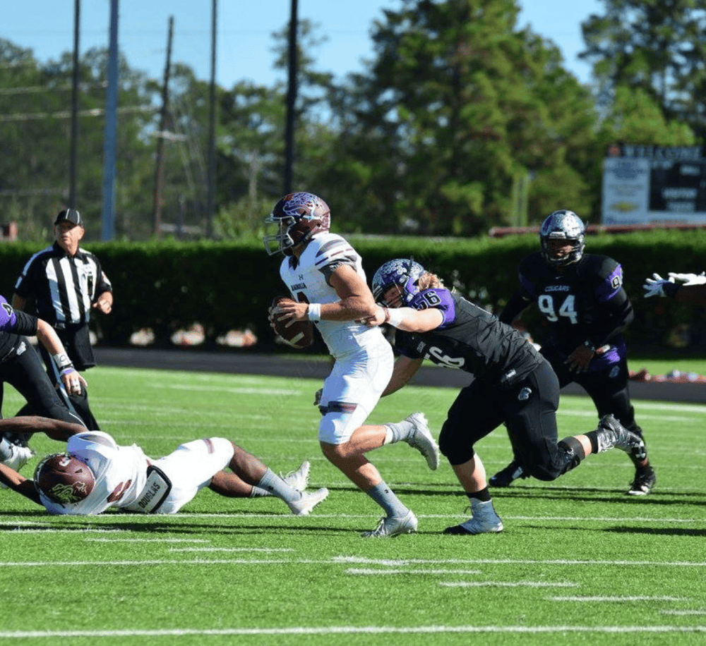 Running back with football in hand tackled by defenders during a high school football game.