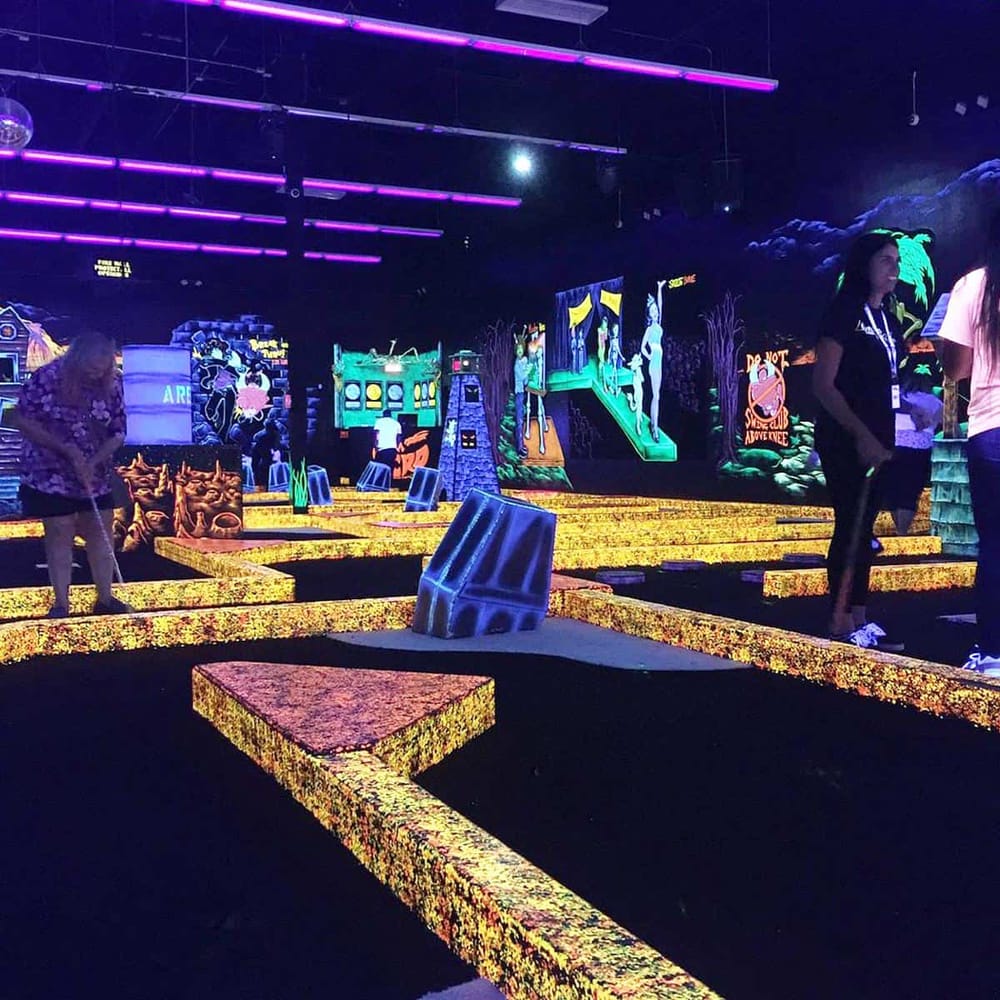 Glow-in-the-dark mini golf course with neon signs and vibrant lighting, perfect for fun indoor adventures.
