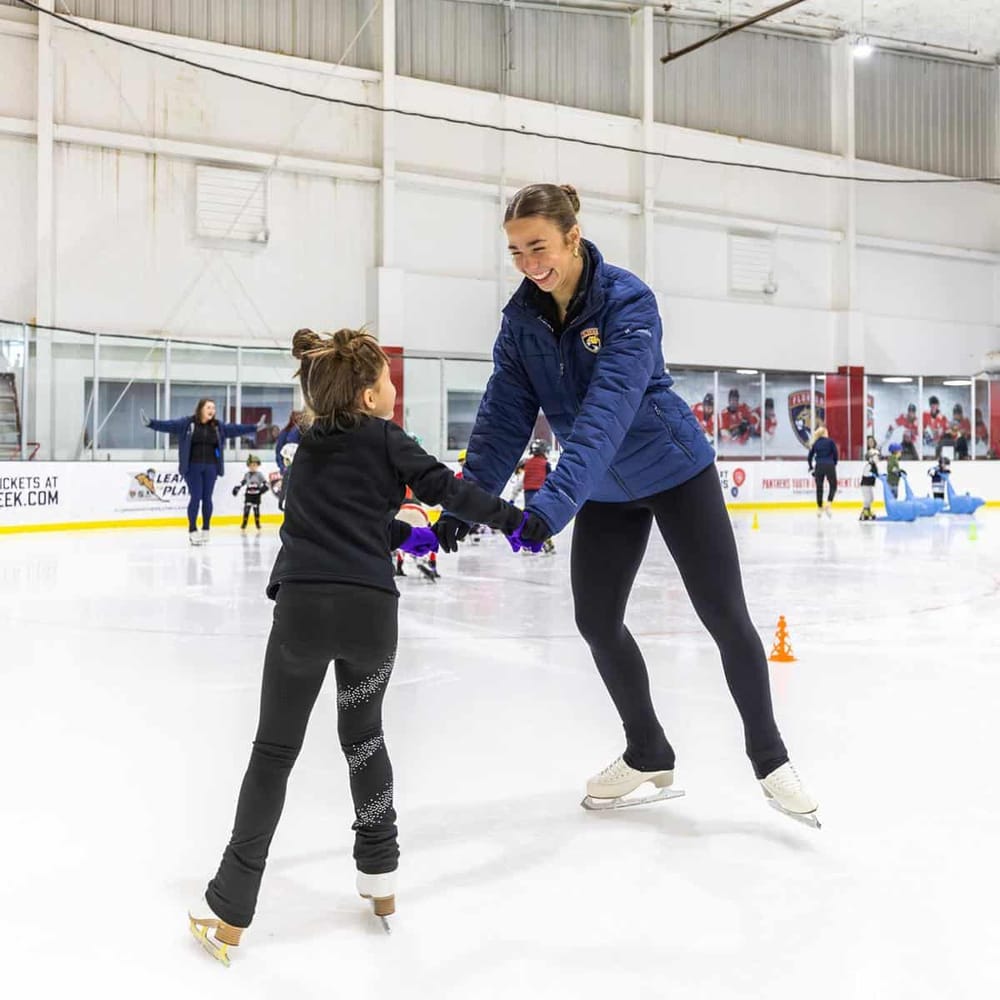 Friendly skating instructor teaching a young girl at indoor ice rink, promoting beginner skating lessons.