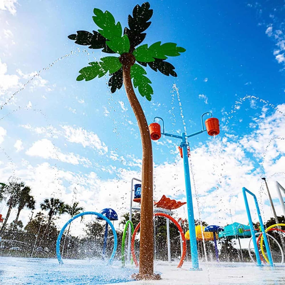 Colorful water park with palm tree-themed sprayer under blue sky, perfect for family fun.
