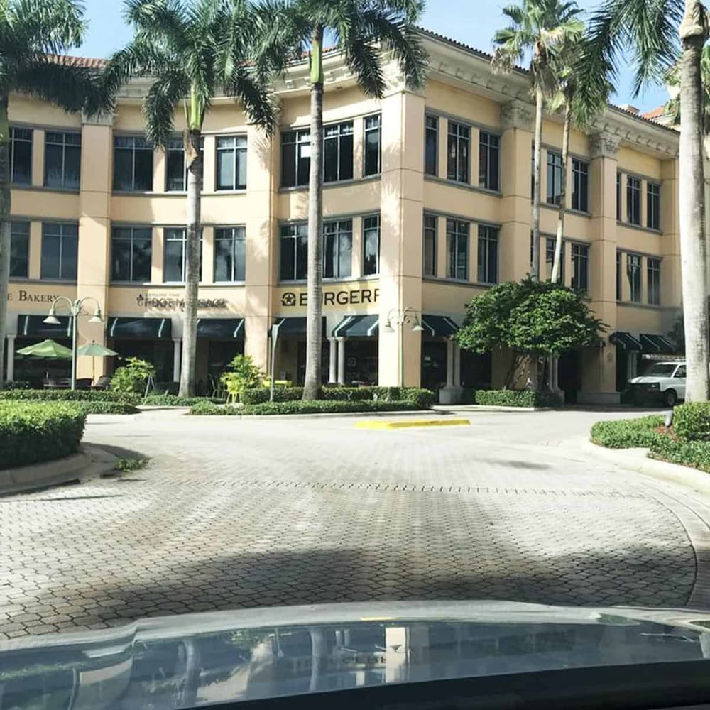 Elegant multi-story building with retail shops and palm trees, showcasing urban shopping and dining in a tropical setting.