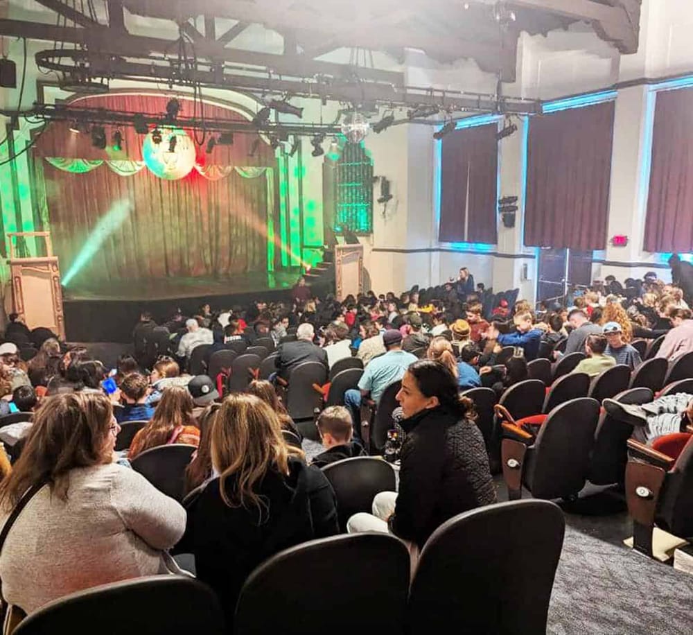 Live comedy show theater with audience, stage lighting, and festive atmosphere.