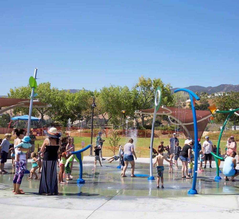 Children enjoying spray park water play area in a sunny outdoor park.