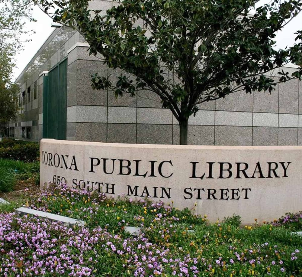 Accessible public library in Corona, South Main Street with welcoming signs and colorful flower landscaping.