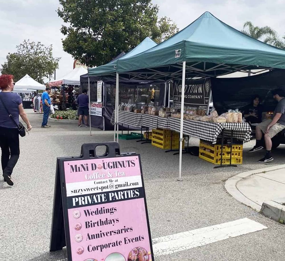 Colorful outdoor farmers market with tents, vendors, and shoppers in a community setting.